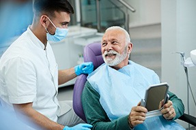 Senior patient looking at dentist while holding small mirror