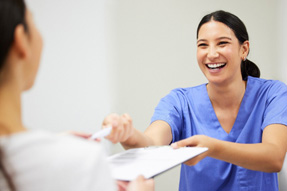 Smiling dental assistant handing patient form
