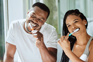 Couple smiling while brushing their teeth in bathroom