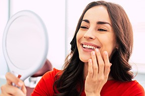 Woman in orange-red shirt smiling at reflection in handheld mirror