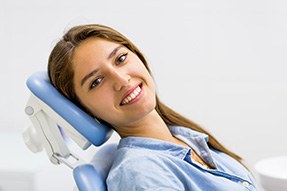 Woman in blue shirt sitting back in dental chair and smiling